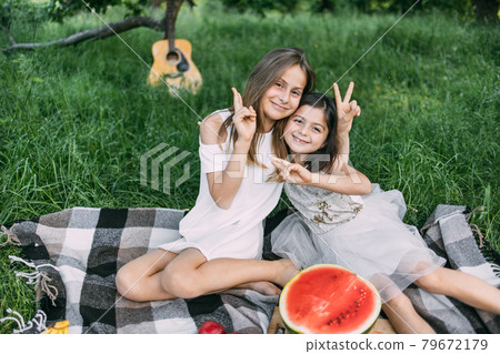 Two cute sisters hugging outdoors during picnic time Two cute sisters hugging outdoors during picnic time 79672179