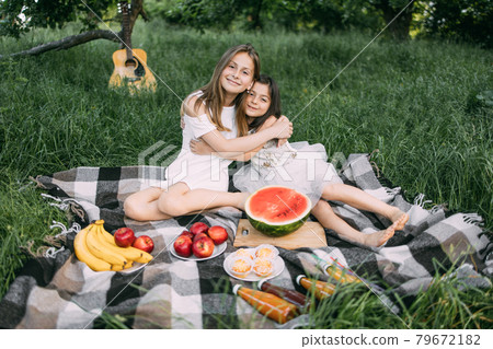 Two cute sisters hugging outdoors during picnic time 79672182