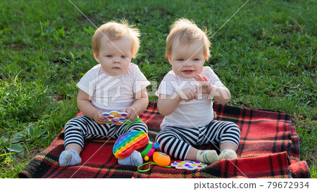 Twin girls play with bright toys on a blanket in a city park 79672934