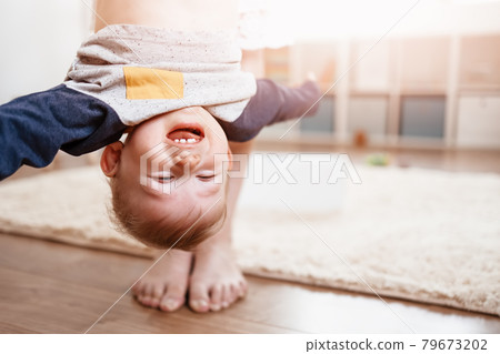 Mother holding upside down her laughing child. Mother holding upside down her laughing child. 79673202