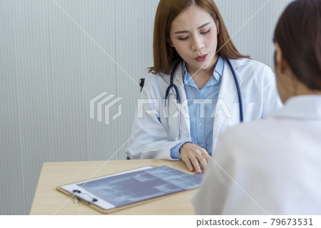 Two asian women doctors discuss meeting doctor's office medical clinic looking x-ray film consulting patient disease. Asian medical lab young women talking together discussing healthcare teamwork Two asian women doctors discuss meeting doctor's office medical clinic looking x-ray film consulting patient disease. Asian medical lab young women talking together discussing healthcare teamwork 79673531