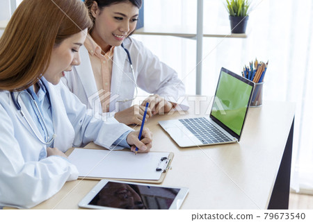 Two asian women doctors discuss meeting doctor's office medical clinic using laptop consulting patient disease. Asian medical lab young women talking together discussing healthcare assistance teamwork 79673540