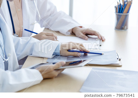 Two asian women doctors discuss meeting doctor's office medical clinic looking x-ray film consulting patient disease. Asian medical lab young women talking together discussing healthcare teamwork 79673541