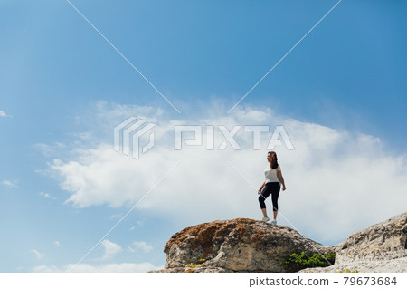 brunette woman standing on a cliff looking at the nature of the journey 79673684