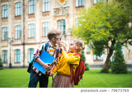 Back to school and education. Little boy kissing girl on the cheek, but girl stop him. No kissing. Social distancing concept. Little students with backpack and notebook 79673769