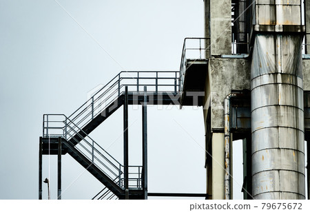 Abstract colourless picture of an iron staircase next to an aluminium pipe at the tower of an industrial plant Abstract colourless picture of an iron staircase next to an aluminium pipe at the tower of an industrial plant 79675672