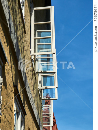 Upward view along a house wall with open windows with white painted window frames in front of a blue sky Upward view along a house wall with open windows with white painted window frames in front of a blue sky 79675674