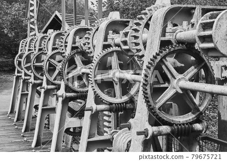 Gear wheels, toothed belts, chains, shafts and racks at a weir on the river Aller, Germany, black and white 79675721