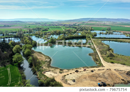 Aerial view of an active gravel pond beside the river Leine near Sarstedt, Germany, with a truck and piles of sand and a village in the background Aerial view of an active gravel pond beside the river Leine near Sarstedt, Germany, with a truck and piles of sand and a village in the background 79675754