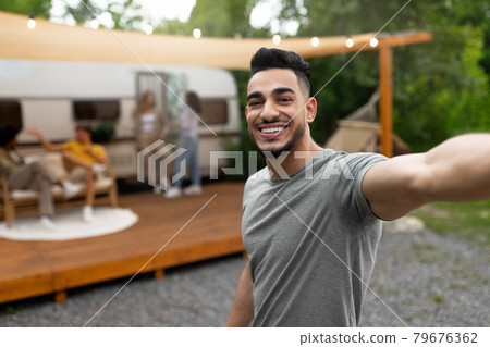 Happy Arab guy taking selfie near motorhome, resting on campsite with multiracial friends, enjoying summer vacation 79676362