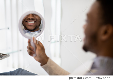 New Smile. Black Man Looking At Mirror While Sitting In Dentist Chair New Smile. Black Man Looking At Mirror While Sitting In Dentist Chair 79676366