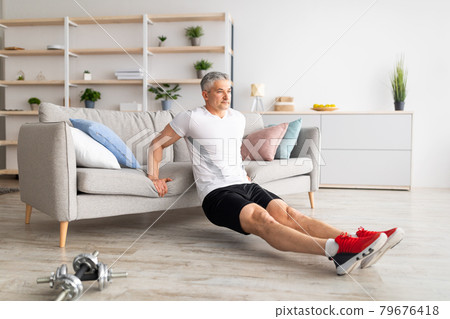 At home workout routine. Sporty mature man leaning on sofa and doing push-up exercises, working out in living room 79676418