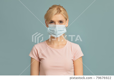 Health care concept. Portrait of young woman wearing surgical mask isolated on grey studio wall background Health care concept. Portrait of young woman wearing surgical mask isolated on grey studio wall background 79676922