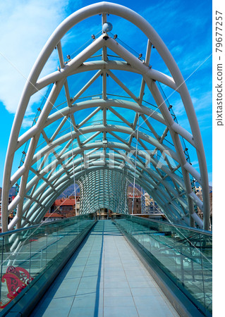Modern stylish design made of glass and metal, pedestrian bridge over the Kura river in Tbilisi Modern stylish design made of glass and metal, pedestrian bridge over the Kura river in Tbilisi 79677257