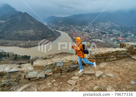 Young girl tourist rejoices posing against the backdrop of an amazing natural landscape. The confluence of two rivers in the city of Mtskheta in Georgia 79677338