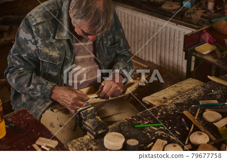 Master-class on making wooden toys. Hands of a wood carving master with a chisel and a wooden workpiece. 79677758