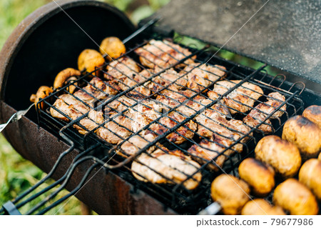 Barbecue with meat and mushrooms fried on the grill outdoors on back yard. Mushrooms on skewers are fried on charcoal Barbecue with meat and mushrooms fried on the grill outdoors on back yard. Mushrooms on skewers are fried on charcoal 79677986