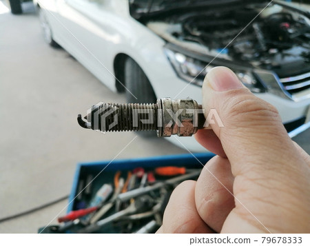 Iridium car spark plug damaged in the mechanic hand with the car blurred background in repair garage 79678333
