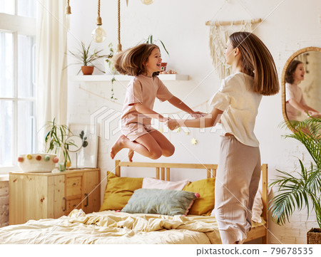 Younger and older caucasian sisters having fun together in bedroom, excited cute little preschool girl jumping on bed Younger and older caucasian sisters having fun together in bedroom, excited cute little preschool girl jumping on bed 79678535
