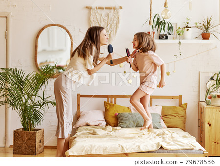 Happy family. Overjoyed younger and older sister singing with hairbrush, looking at each other and smiling Happy family. Overjoyed younger and older sister singing with hairbrush, looking at each other and smiling 79678536