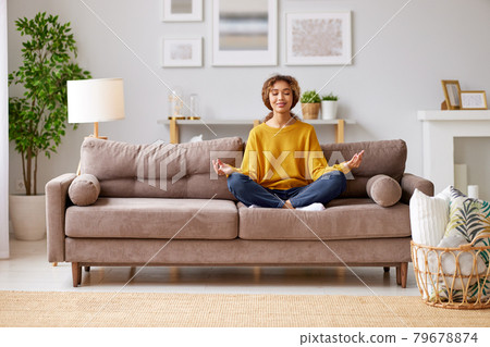 Young mixed race woman meditating with closed eyes  in living room at home 79678874