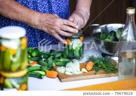 Senior woman or grandmother homemade canning the fresh, bio cucumbers to a jars with onion, carrot and dill, food concept 79679028