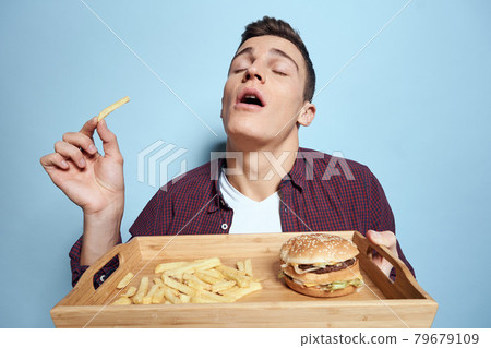 Man with wooden pallet fast food french fries hamburger hunger diet food blue background Man with wooden pallet fast food french fries hamburger hunger diet food blue background 79679109