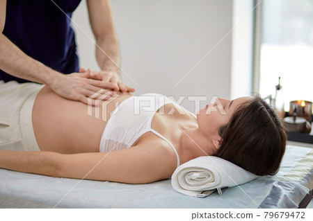 Male hands of massage therapist making light massage to the belly of pregnant female 79679472