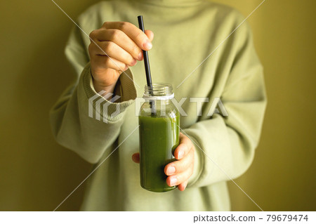 A woman is holding a bottle of green freshly squeezed vegetable or fruit juice. A woman is holding a bottle of green freshly squeezed vegetable or fruit juice. 79679474