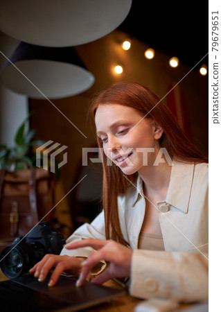 Positive redhead female designer working on marketing project at cafe, smiling Positive redhead female designer working on marketing project at cafe, smiling 79679651