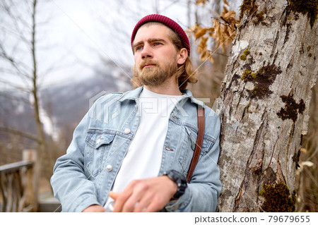 Dreamy caucasian traveler in denim jacket near tree in spring weather, looking at side Dreamy caucasian traveler in denim jacket near tree in spring weather, looking at side 79679655