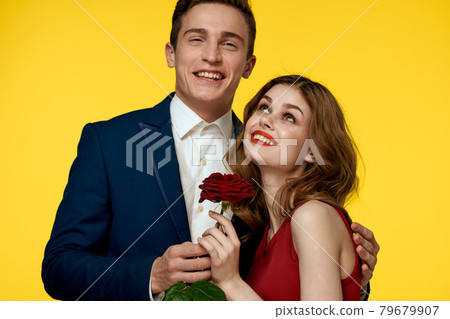 A romantic man hugs a woman in a red dress with a rose in his hand on a yellow background A romantic man hugs a woman in a red dress with a rose in his hand on a yellow background 79679907