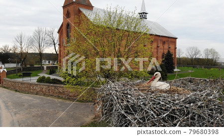 A stork sits in a nest against the backdrop of a church. View from the drone. A stork sits in a nest against the backdrop of a church. View from the drone. 79680398