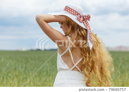 Girl in a white dress and hat on a field background. 79680757