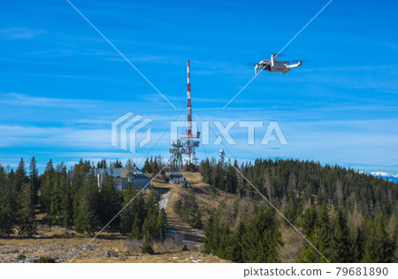 White drone with photo camera flying in the blue sky and telecommunication tower in the background 79681890