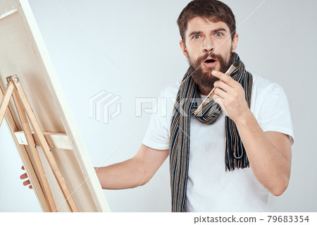 A man artist draws on an easel a scarf white t-shirt art hobby creativity A man artist draws on an easel a scarf white t-shirt art hobby creativity 79683354