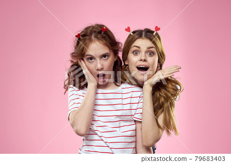 Happy sisters are having fun on a pink background and heart-shaped clothespins on their heads Happy sisters are having fun on a pink background and heart-shaped clothespins on their heads 79683403