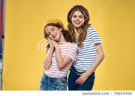 Cheerful sisters in hats striped T-shirts joy lifestyle yellow background family Cheerful sisters in hats striped T-shirts joy lifestyle yellow background family 79683406