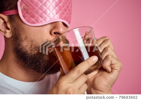 A man in a pink sleep mask with a cup of tea in his hands on an isolated background cropped view A man in a pink sleep mask with a cup of tea in his hands on an isolated background cropped view 79683602