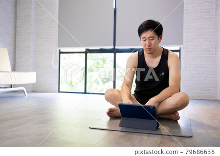 Young man exercising at home while watching a video tutorial on tablet. Male fitness guy training indoors online Young man exercising at home while watching a video tutorial on tablet. Male fitness guy training indoors online 79686638