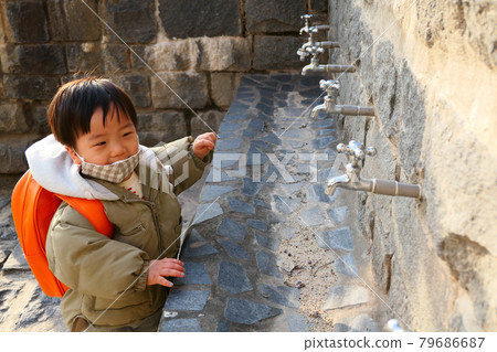 A child playing at the faucet with a bag on his back A child playing at the faucet with a bag on his back 79686687
