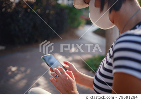A woman wearing a protective mask looks at her smartphone display A woman wearing a protective mask looks at her smartphone display 79691284