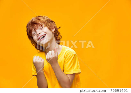 Expressive red-haired boy gestures with his hands yellow isolated background holds his hands in fists  79691491