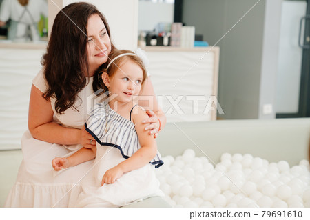 mother and daughter sit by the dry pool with white balls. playroom for children mother and daughter sit by the dry pool with white balls. playroom for children 79691610