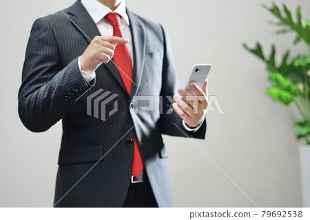 A businessman operating a smartphone 79692538
