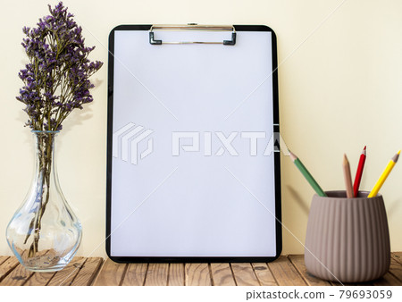 Plain Office Clipboard With Stack Of Pens In A Holder Beside A Flower Vase. Empty Paper Sheet With Colorful Pencils Next To Floret Container Placed On Table. Plain Office Clipboard With Stack Of Pens In A Holder Beside A Flower Vase. Empty Paper Sheet With Colorful Pencils Next To Floret Container Placed On Table. 79693059