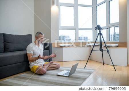 A mature man in white tshirt doing yoga tutorial online 79694003