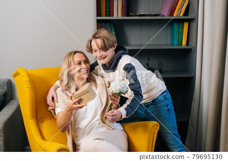 Portrait of smiling loving kid child son hugging kissing happy young mom congratulating with mothers day. Portrait of smiling loving kid child son hugging kissing happy young mom congratulating with mothers day. 79695130