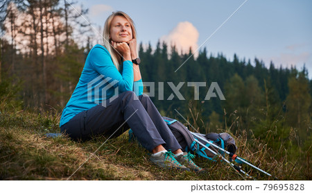 Beautiful young woman traveler sitting on grassy hill. Beautiful young woman traveler sitting on grassy hill. 79695828