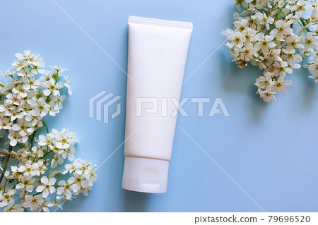 Unbranded white cosmetic squeeze tube and spring white flowers of bird cherry on blue background. Mockup, template. Container for body lotion, moisturizer cream, shower gel, shaving cream. 79696520